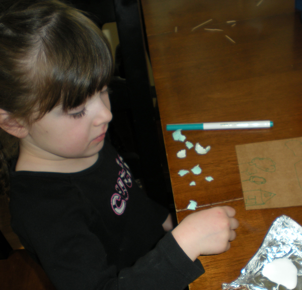 Girl breaking eggshell pieces at a table beside a sketched cardstock design