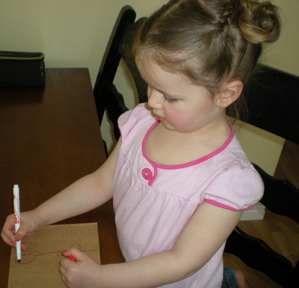Young girl in pink sketching a design with a red marker on cardstock